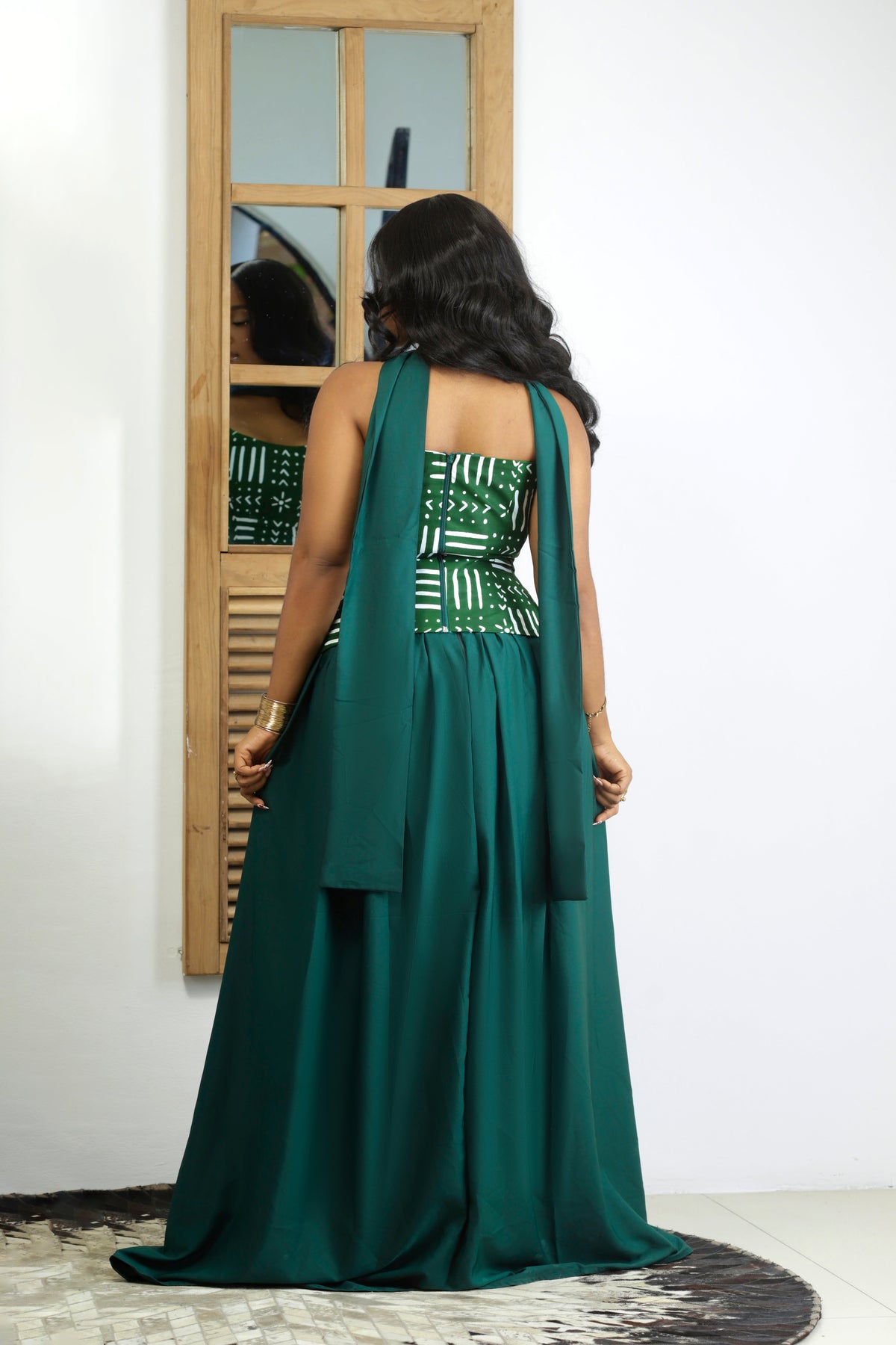 Back view of the Miraya Set showing the structured mud-cloth print corset top in emerald green with white linear and arrow motifs, a long draping neck scarf, and a full-length satin-finish skirt with a sweeping hem.
